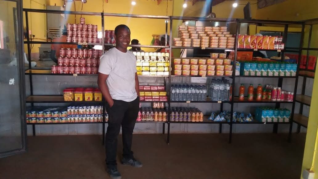 Feliciano de pé numa loja, diante de prateleiras com produtos alimentares e bebidas