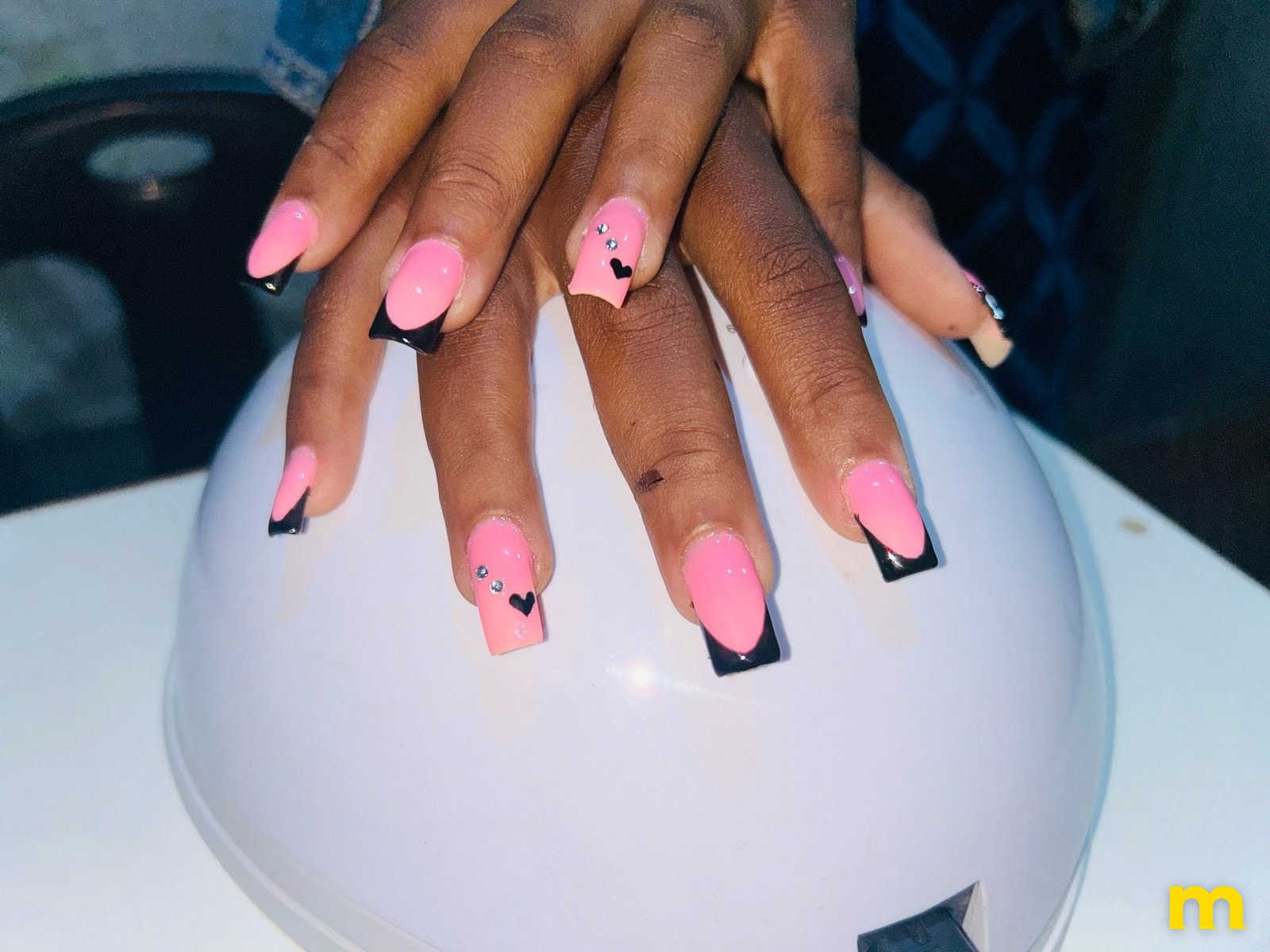 Unhas cor-de-rosa com pontas pretas, pequenos corações e brilhantes, pintadas pelo Nélio